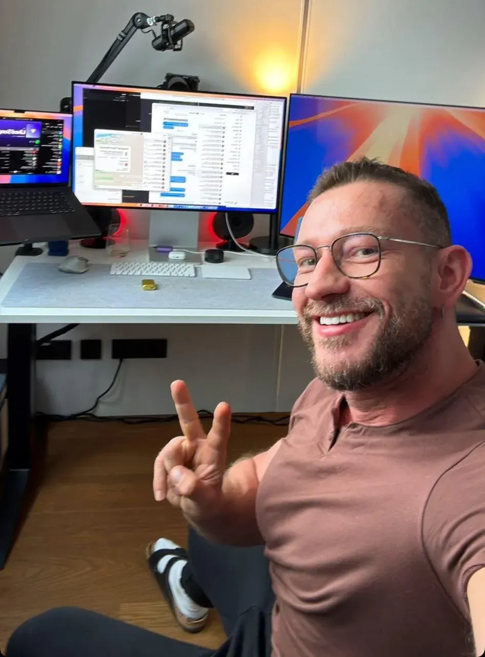 Man taking a selfie in a home office with dual monitors, a laptop and desk accessories for share structure advisory content